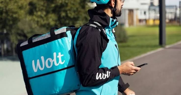 Wolt dostavljač s plavom termo torbom vozi biciklom i gleda u mobitel