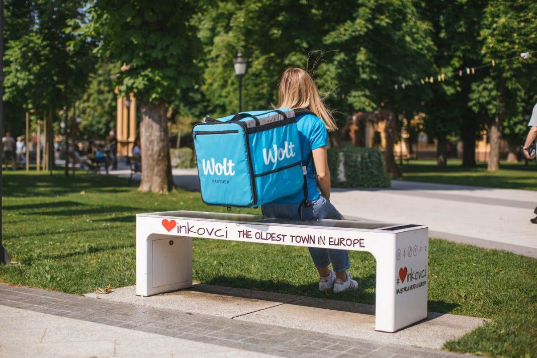 Wolt dostavljačica s torbom sjedi na klupi u parku između narudžbi
